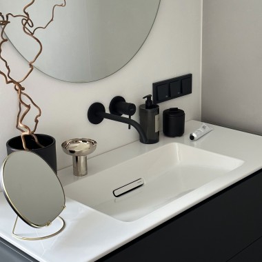 Ein runder Spiegel über dem Waschtisch fügt sich gut unter der Dachschräge ein, schwarze Armaturen ergänzen den klaren, modernen Look. (© C’est Design Studio)
