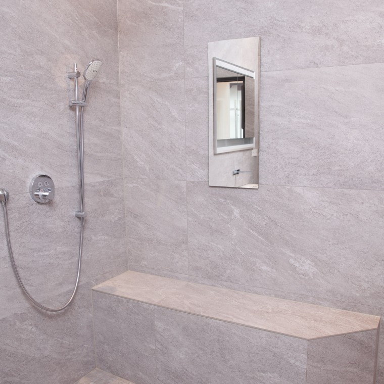 Ansicht der bodenebenen Dusche mit Sitzmöglichkeit und der verspiegelten Geberit Schiebetür.
