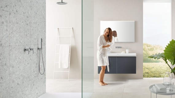 Frau trocknet sich Haare mit Handtuch in Bad mit offener Dusche und großen Fliesen im Terrazzo-Stil