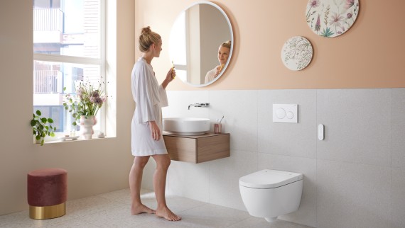 Frau in Badezimmer mit Geberit AquaClean Alba, einer preiswerten Toilette mit Waschfunktion Frau in Badezimmer mit Geberit AquaClean Alba, einer preiswerten Toilette mit Waschfunktion
