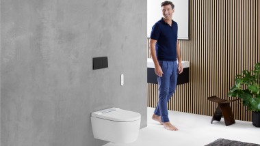 Mann im Badezimmer schaut auf den WC-Bereich, in dem eine Toilette von Geberit steht.