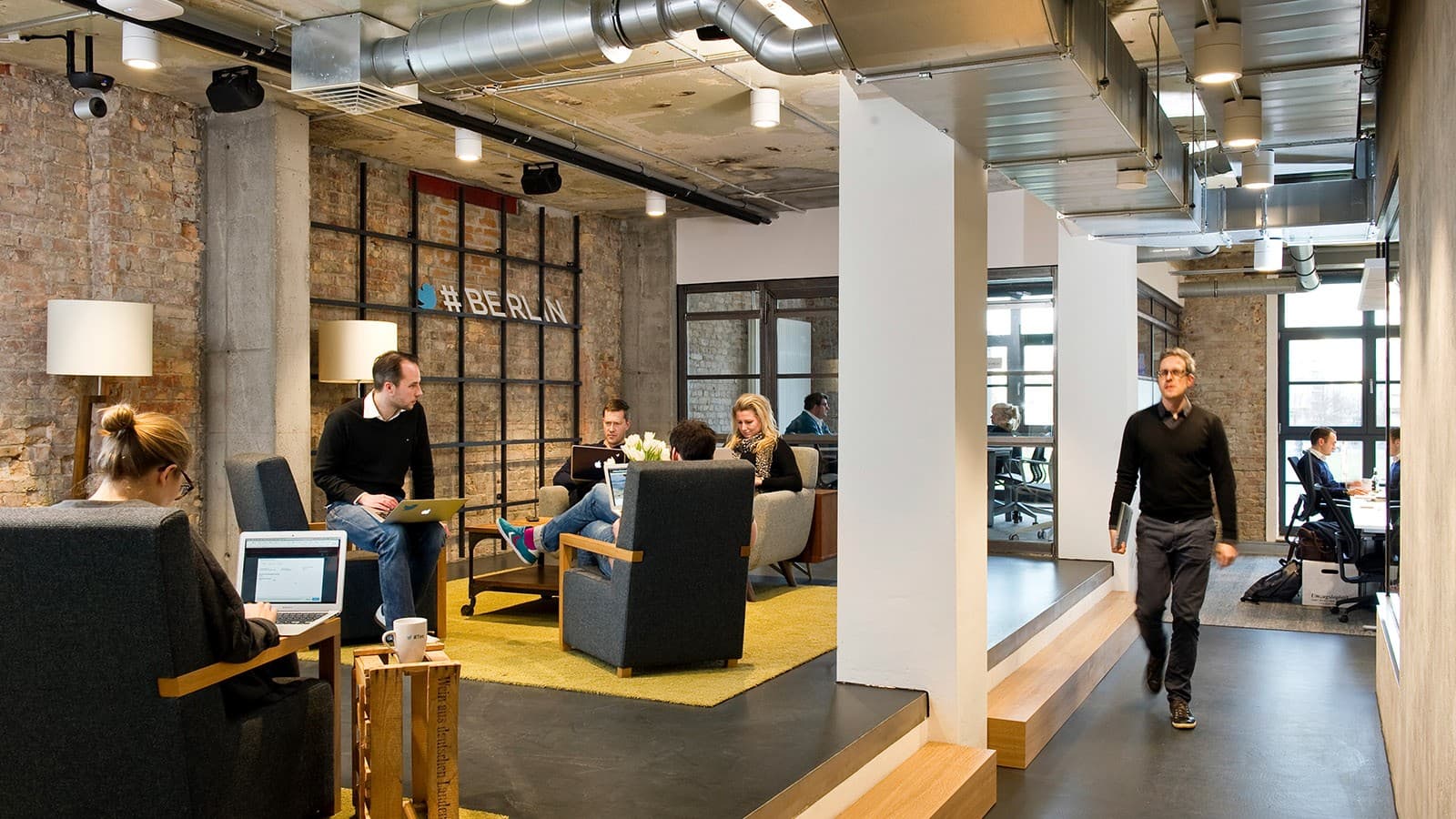 Mitarbeiter der Berliner Twitter-Zentrale arbeiten vor einer Wand, die Teil der ehemaligen Berliner Mauer ist. Mitarbeiter der Berliner Twitter-Zentrale arbeiten vor einer Wand, die Teil der ehemaligen Berliner Mauer ist.